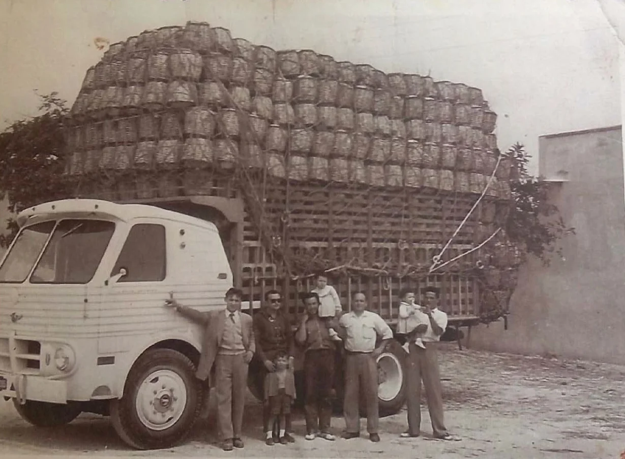Historia de Cestería Aparici en 1956: Juan Domenech y Mercedes Domenech junto a camión de transporte de capazos artesanales en Aielo de Malferit.
